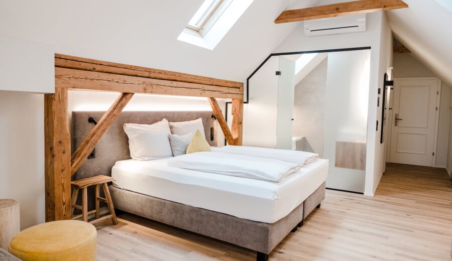 A double bed photographed from the side and illuminated by the skylight, while the sliding door to the bathroom can be seen in the background.