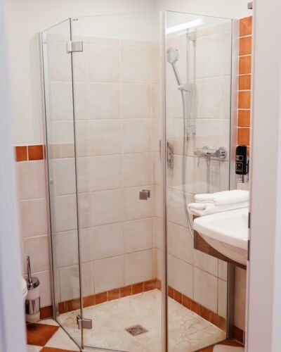 See-through shower in the bathroom with white and orange tiles at Hotel Kirchbichl