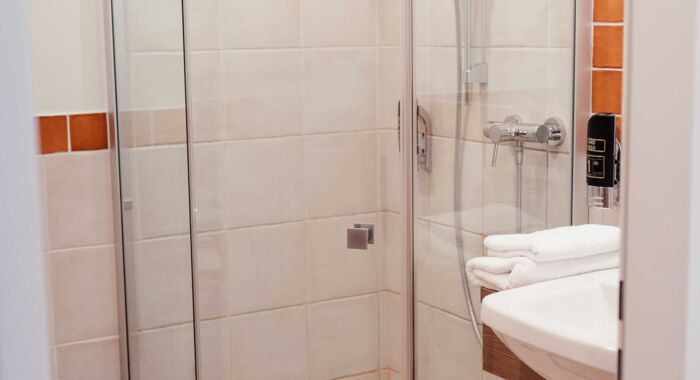 Durchsichtige Dusche im Badezimmer mit weißen und orangefarbenen Fliesen im Hotel Kirchbichl
