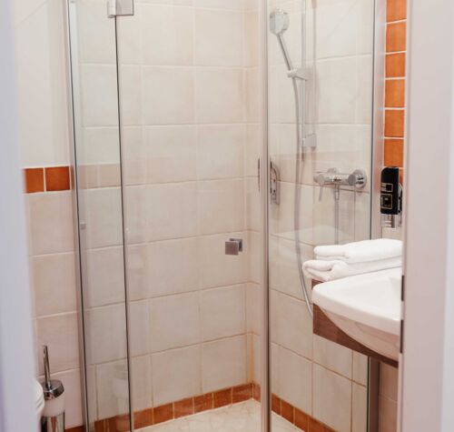 Durchsichtige Dusche im Badezimmer mit weißen und orangefarbenen Fliesen im Hotel Kirchbichl