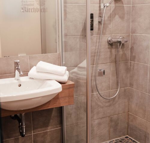 Eine Walk-In Dusche und ein Waschbecken im Badezimmer des Twinzimmers im 4-Sterne Hotel Kirchbichl