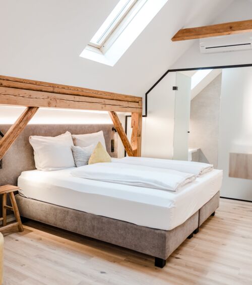 A double bed photographed from the side and illuminated by the skylight, while the sliding door to the bathroom can be seen in the background.
